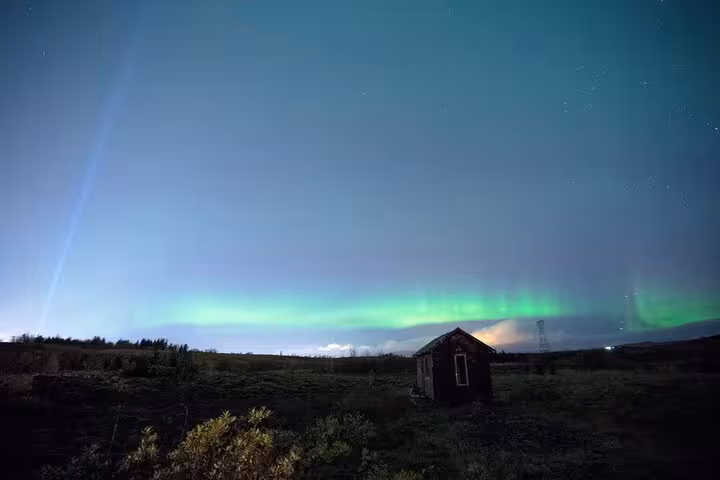 Aurora borealis glowing green over a remote Icelandic cabin at night near Reykjavik