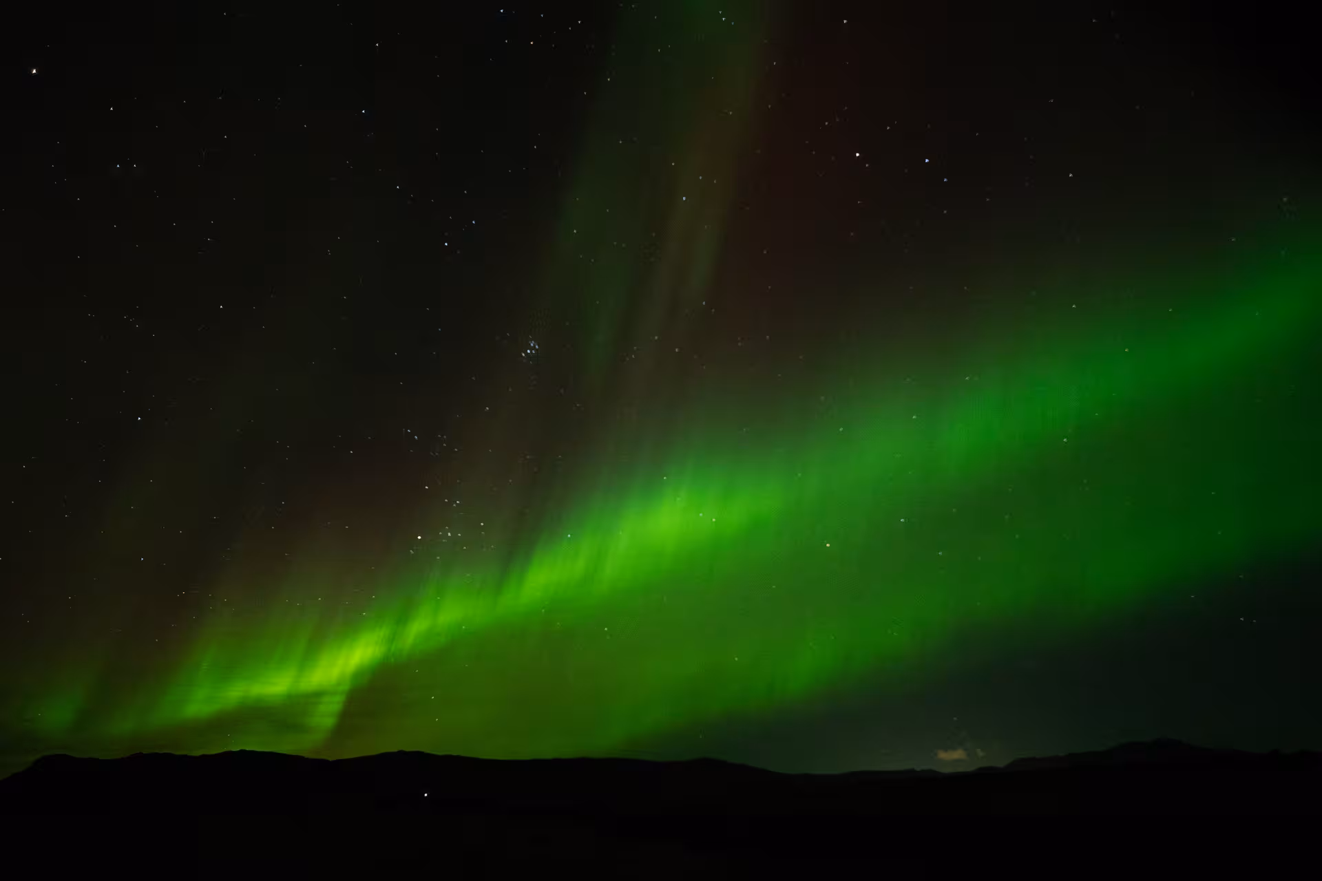 Vibrant green northern lights aurora borealis dancing over dark mountain silhouettes in Iceland night sky