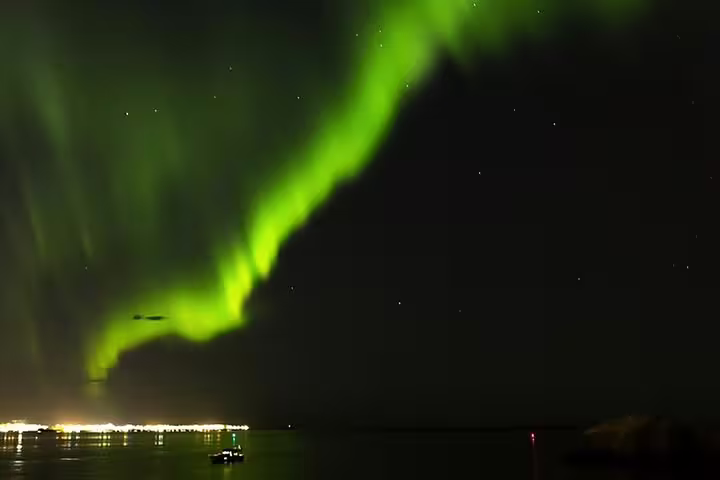 Vivid green northern lights aurora borealis over Reykjavik harbor waters at night