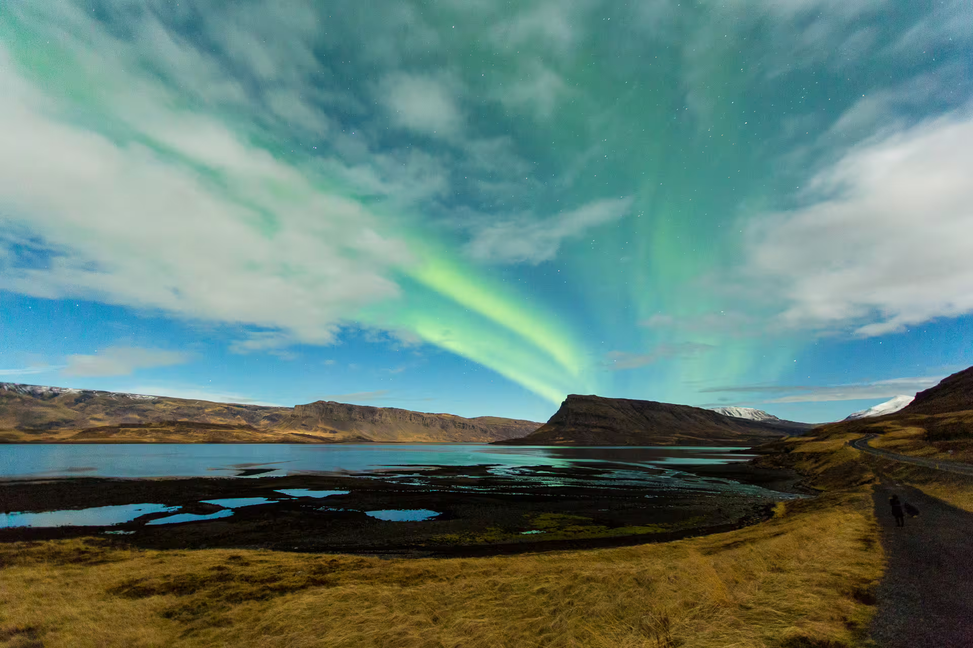 Aurora borealis green northern lights over Icelandic fjord with mountains and a lone silhouette at night