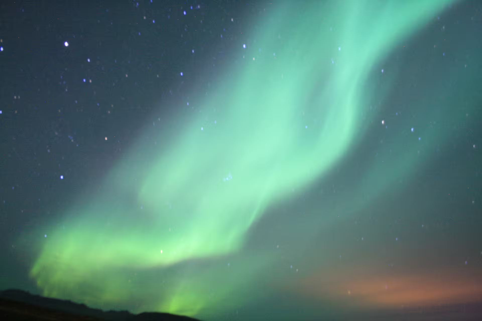 Vibrant green aurora borealis swirling over dark Icelandic hills and starry night sky
