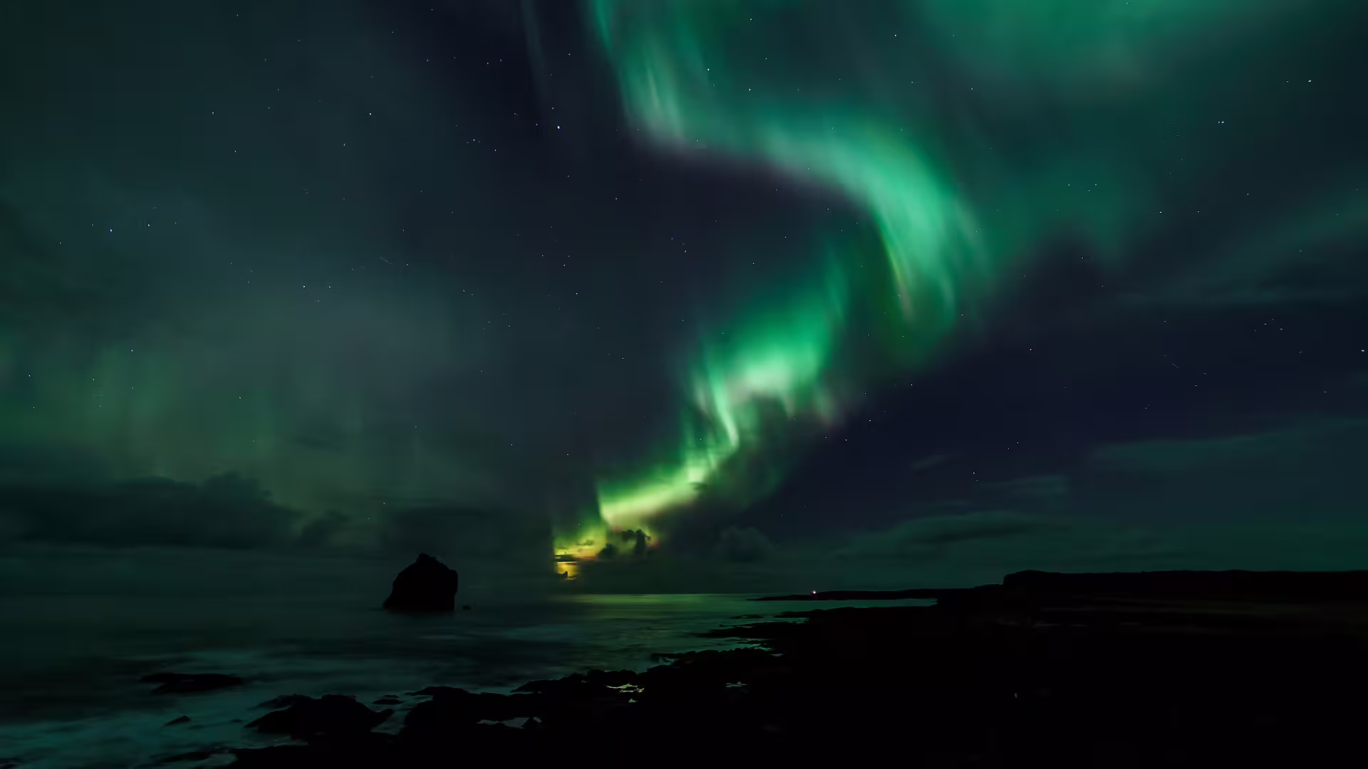 Aurora borealis northern lights swirling over rocky Iceland coastline and dark ocean at night