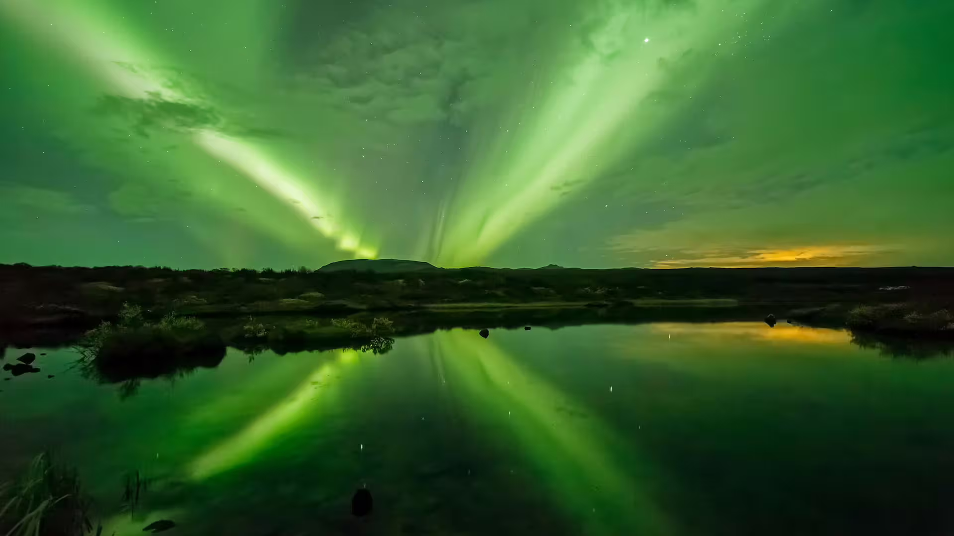 Vivid green northern lights reflecting over a calm lake in Reykjavik, Iceland at night
