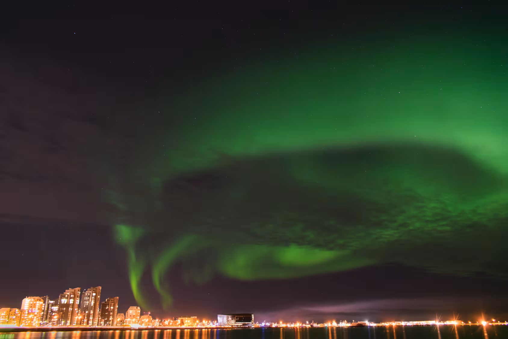 Vibrant Northern Lights over Reykjavik skyline during Iceland stopover tour, showcasing natural beauty and city lights.