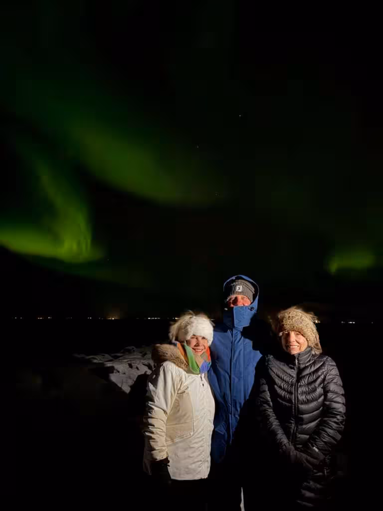 Three tourists posing under vibrant green northern lights aurora borealis in Iceland at night