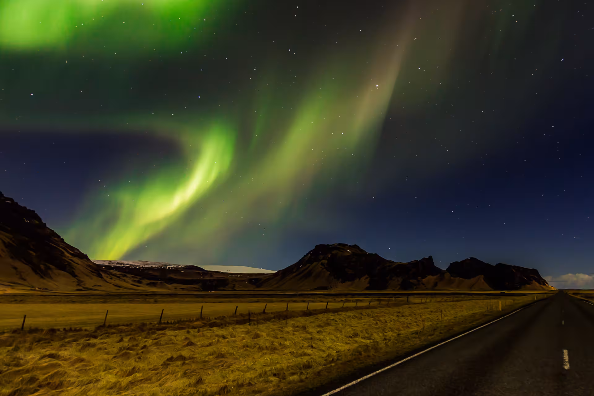 Vivid green northern lights swirling over a mountain road in Iceland at night