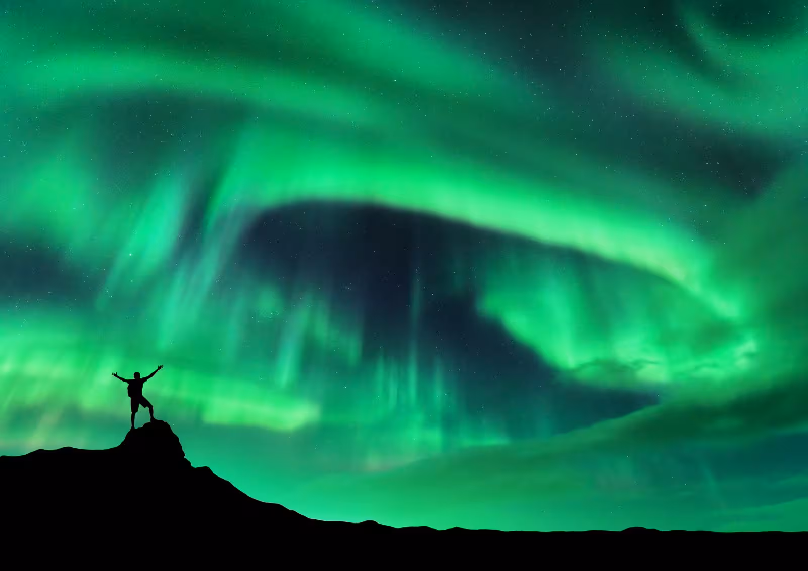 Traveler silhouetted against vibrant Northern Lights, a must-see on the 5-Day Northern Lights Hunt & Glacier Lagoon Tour.