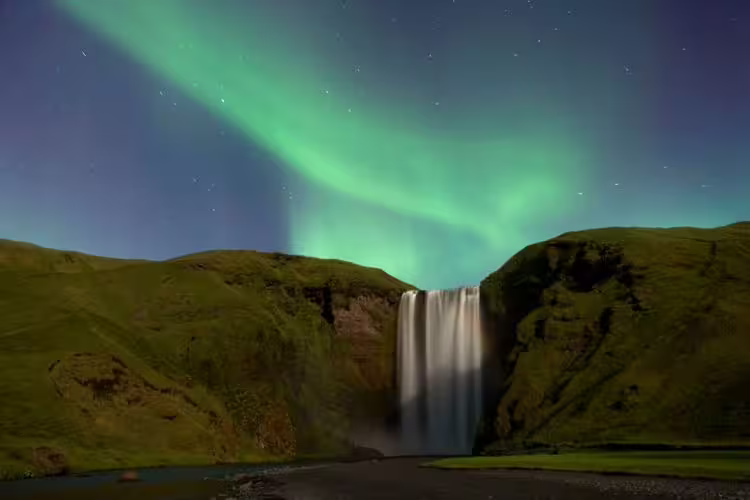 Aurora borealis dancing over Skógafoss waterfall in Iceland at night with green northern lights