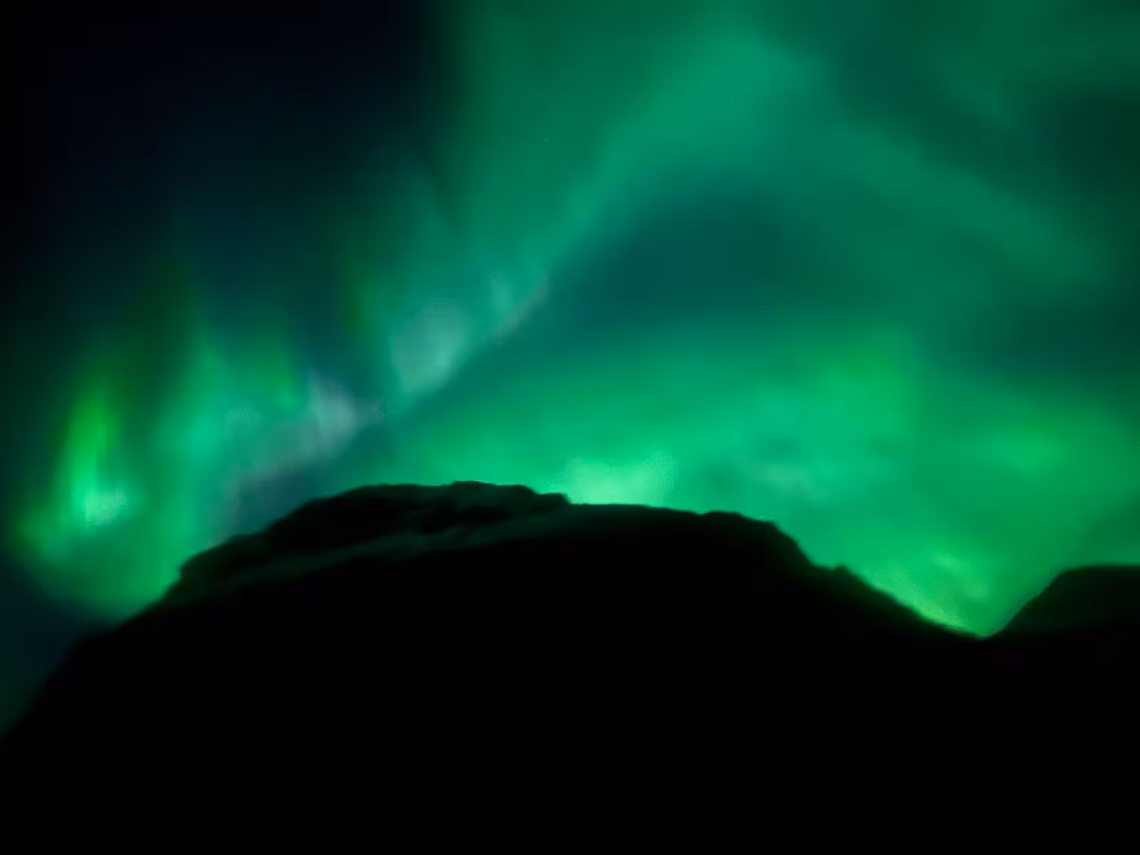 Vibrant green northern lights aurora borealis over dark mountain silhouette on Snaefellsnes Peninsula