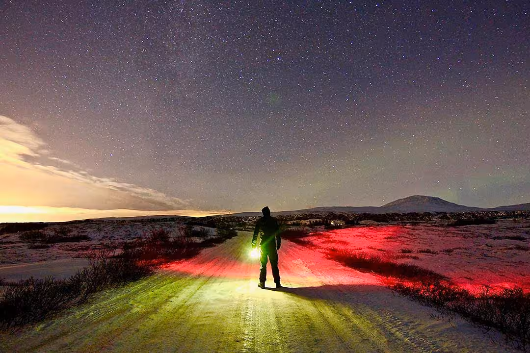 Guide with headlamp on a snowy road beneath a brilliant starry sky, Northern Lights and stargazing tour adventure