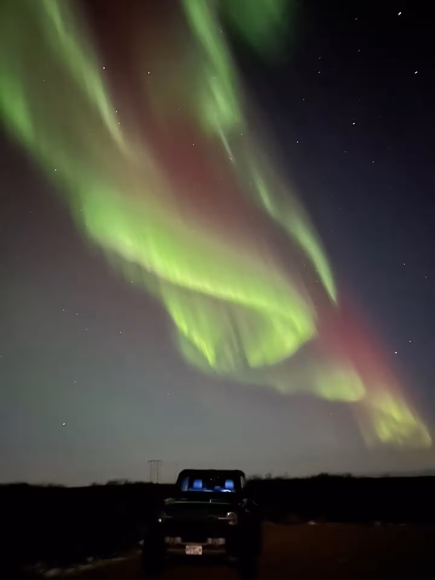 Vibrant green and red northern lights aurora borealis over a super jeep on a dark Iceland landscape