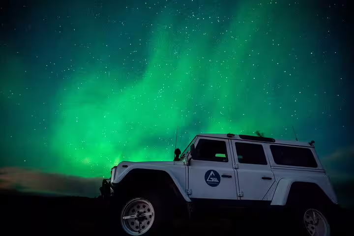 White super jeep under vibrant green northern lights aurora borealis in Iceland night sky
