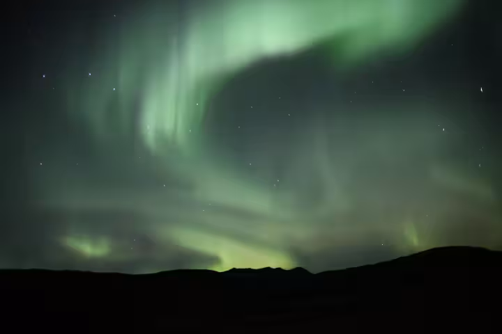Vibrant green northern lights swirling over dark Icelandic hills at night
