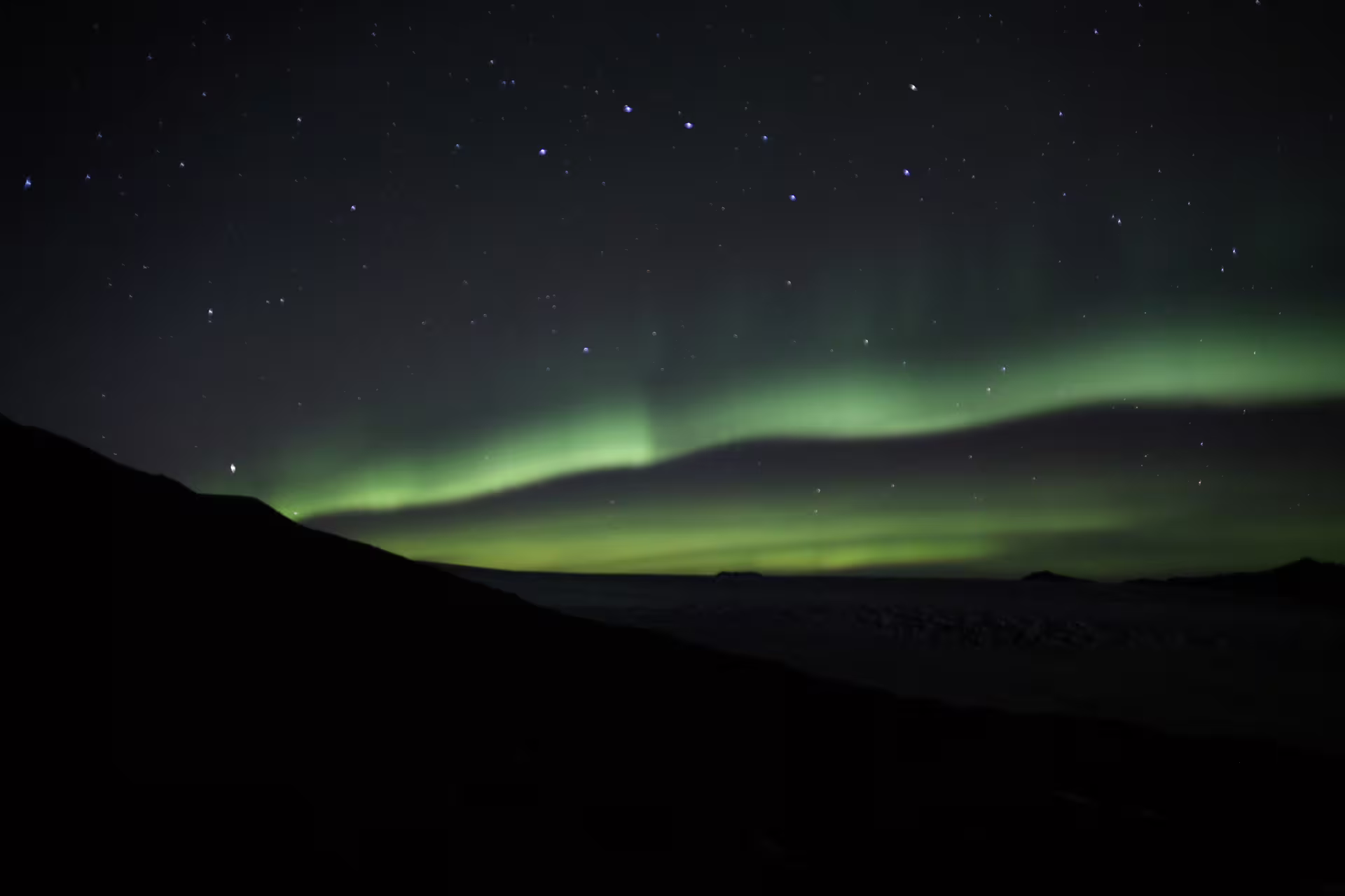 Aurora borealis green northern lights over dark mountain silhouettes in Iceland night sky