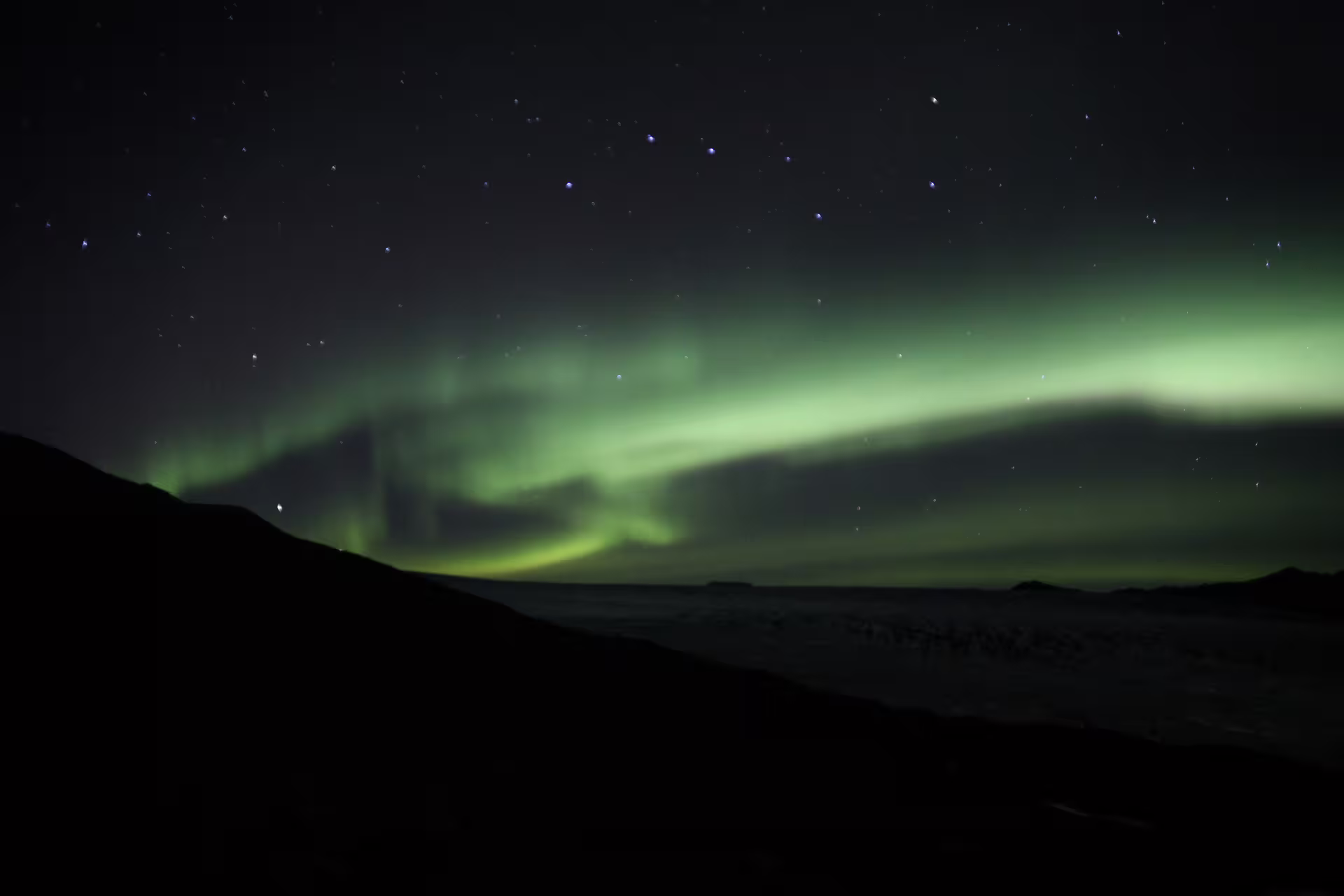 Vivid green aurora borealis arching over dark Icelandic mountain silhouettes under a starry night sky