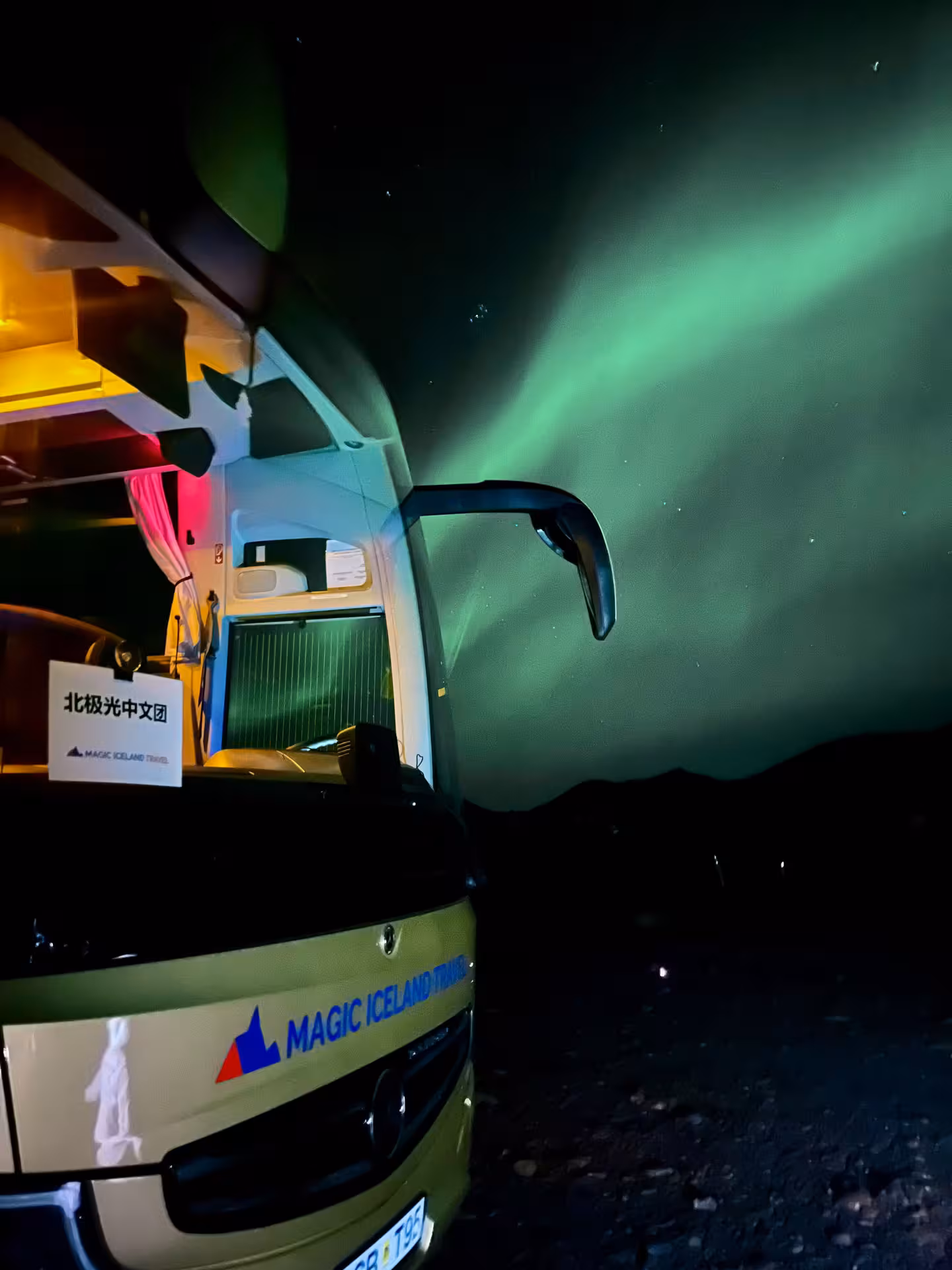 Magic Iceland Travel bus parked under vivid green northern lights aurora borealis in Iceland night sky