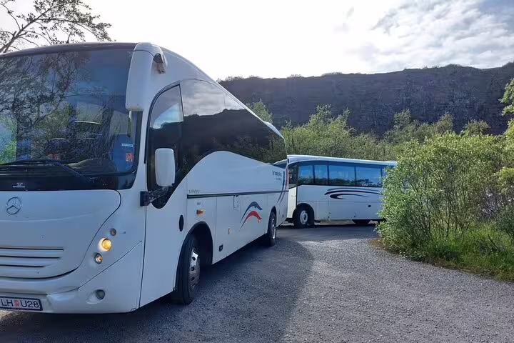 Two white Mercedes coach buses parked on gravel road surrounded by green hills in Akureyri, Iceland