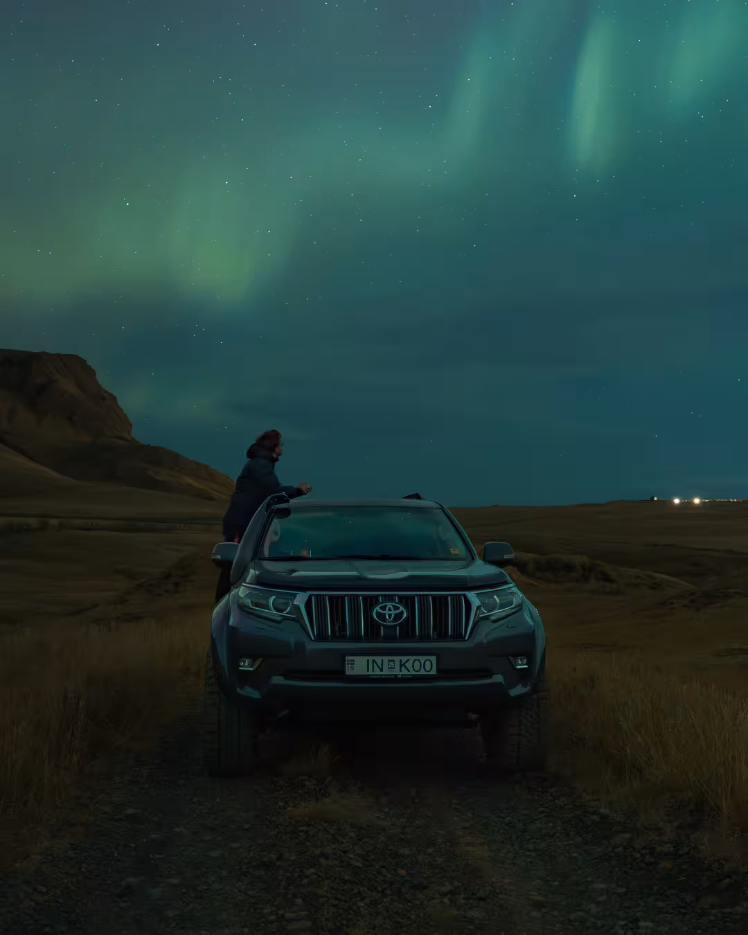Traveler beside 4x4 under green aurora in Iceland countryside, Northern Lights tour with expert guide