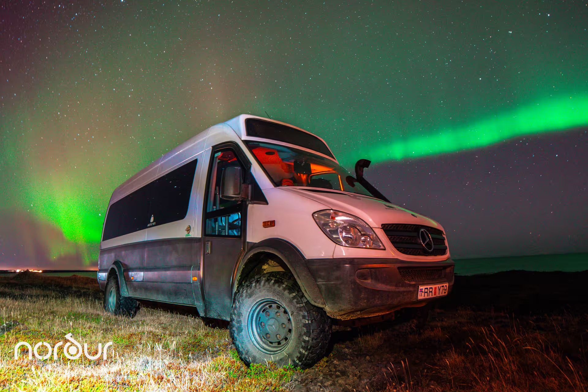 Private 4x4 Mercedes Sprinter van parked under vivid green northern lights aurora on Iceland night tour from Reykjavik.