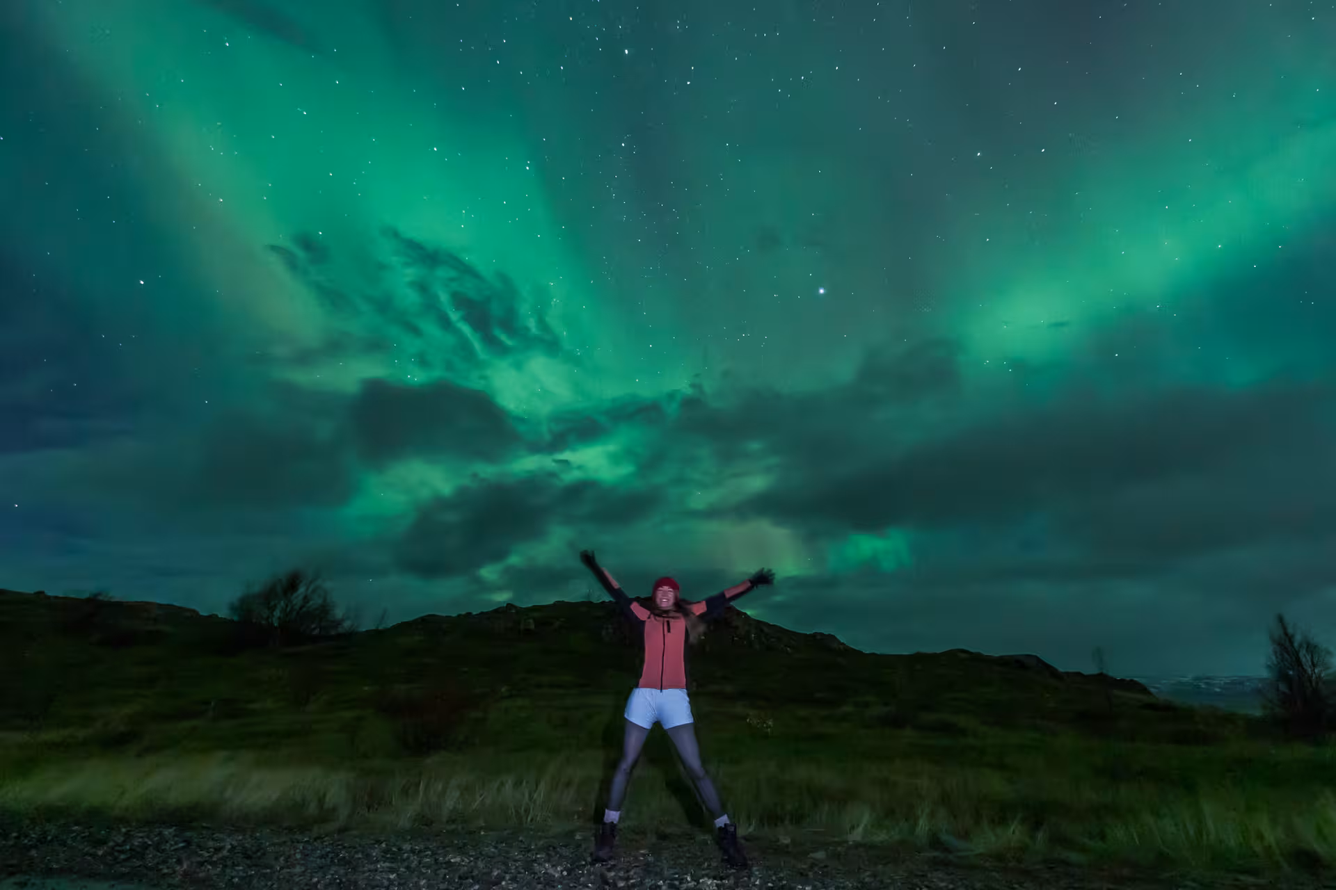 Person celebrating under vibrant green northern lights aurora borealis in Iceland at night