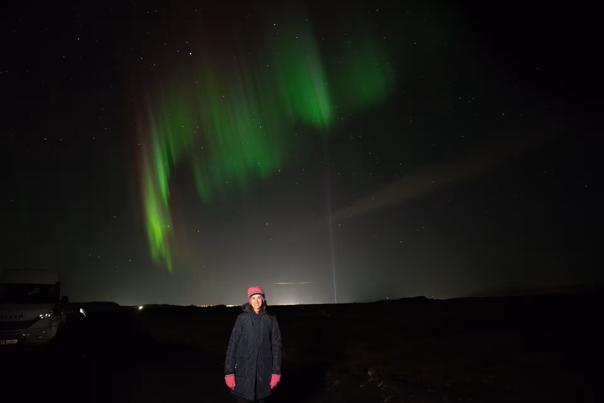 Woman smiling under vivid green northern lights aurora borealis in Iceland night sky