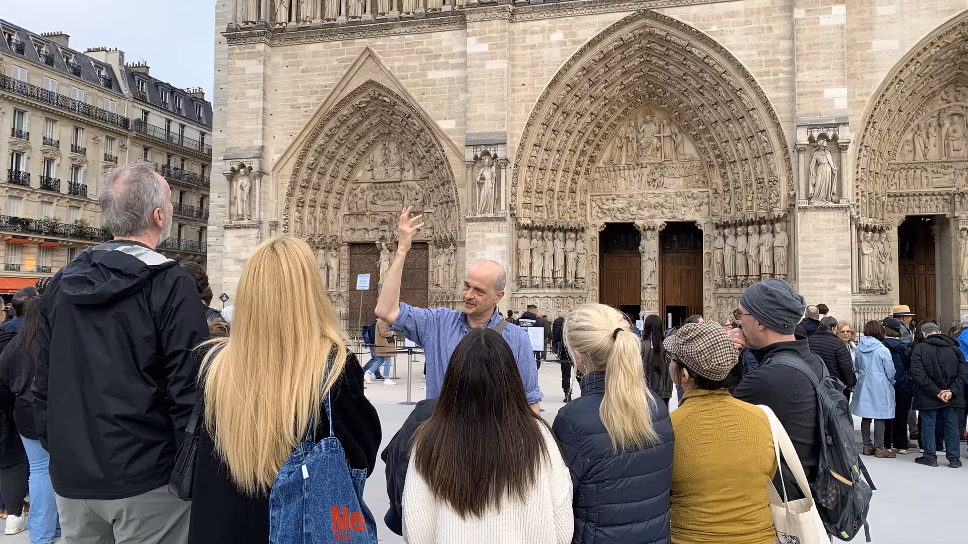 Tour guide gesturing to Notre-Dame Cathedral facade with group of tourists on Ile de la Cite, Paris