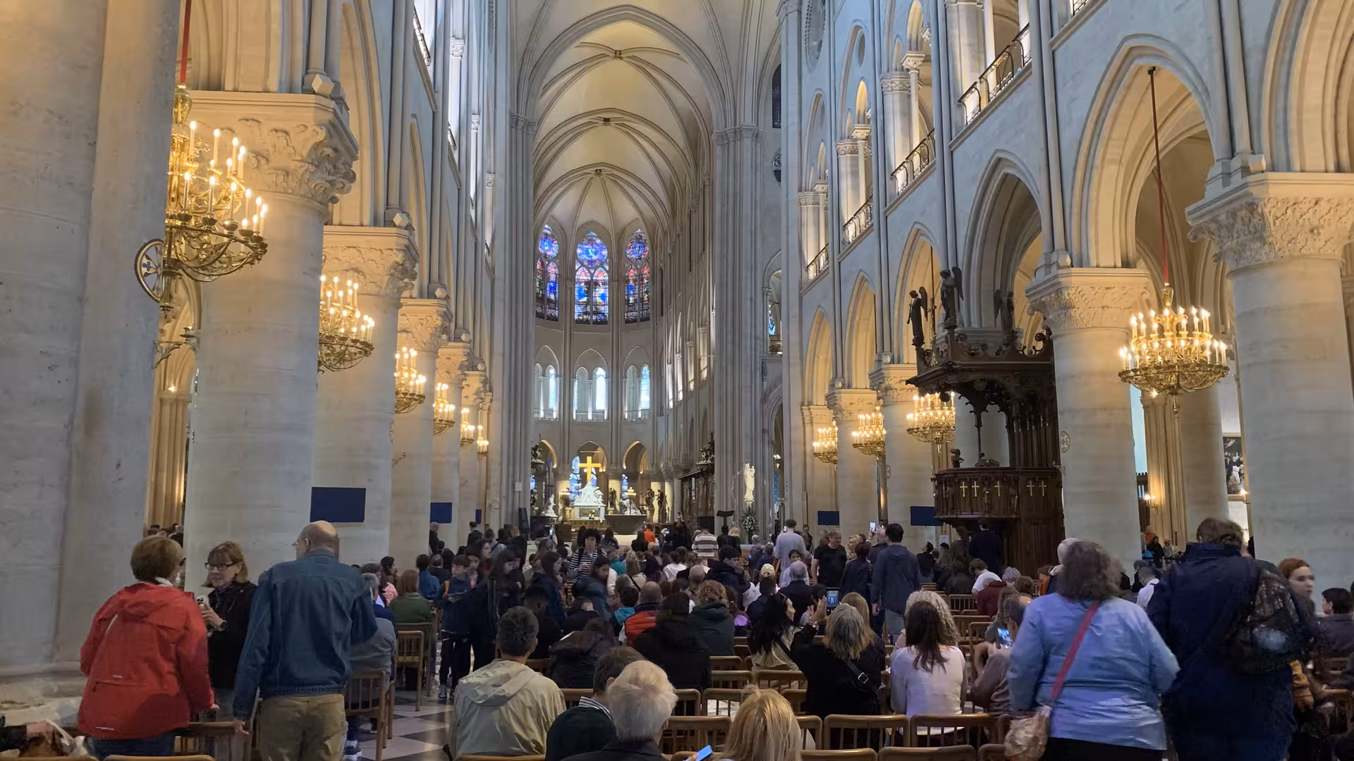 Crowded interior of Notre-Dame Cathedral Paris showing gothic arches, chandeliers, and stained glass windows