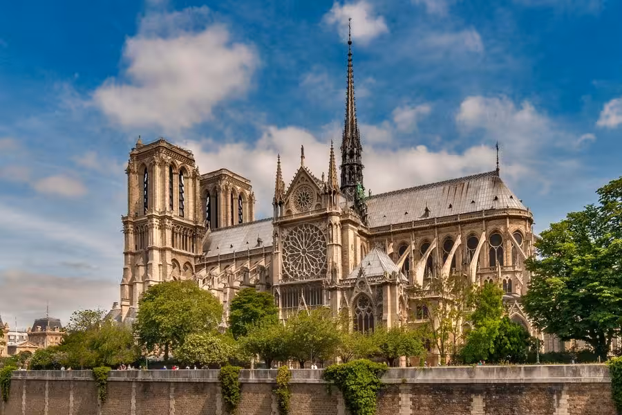 Notre-Dame Cathedral in Paris with Gothic spire and flying buttresses under blue sky