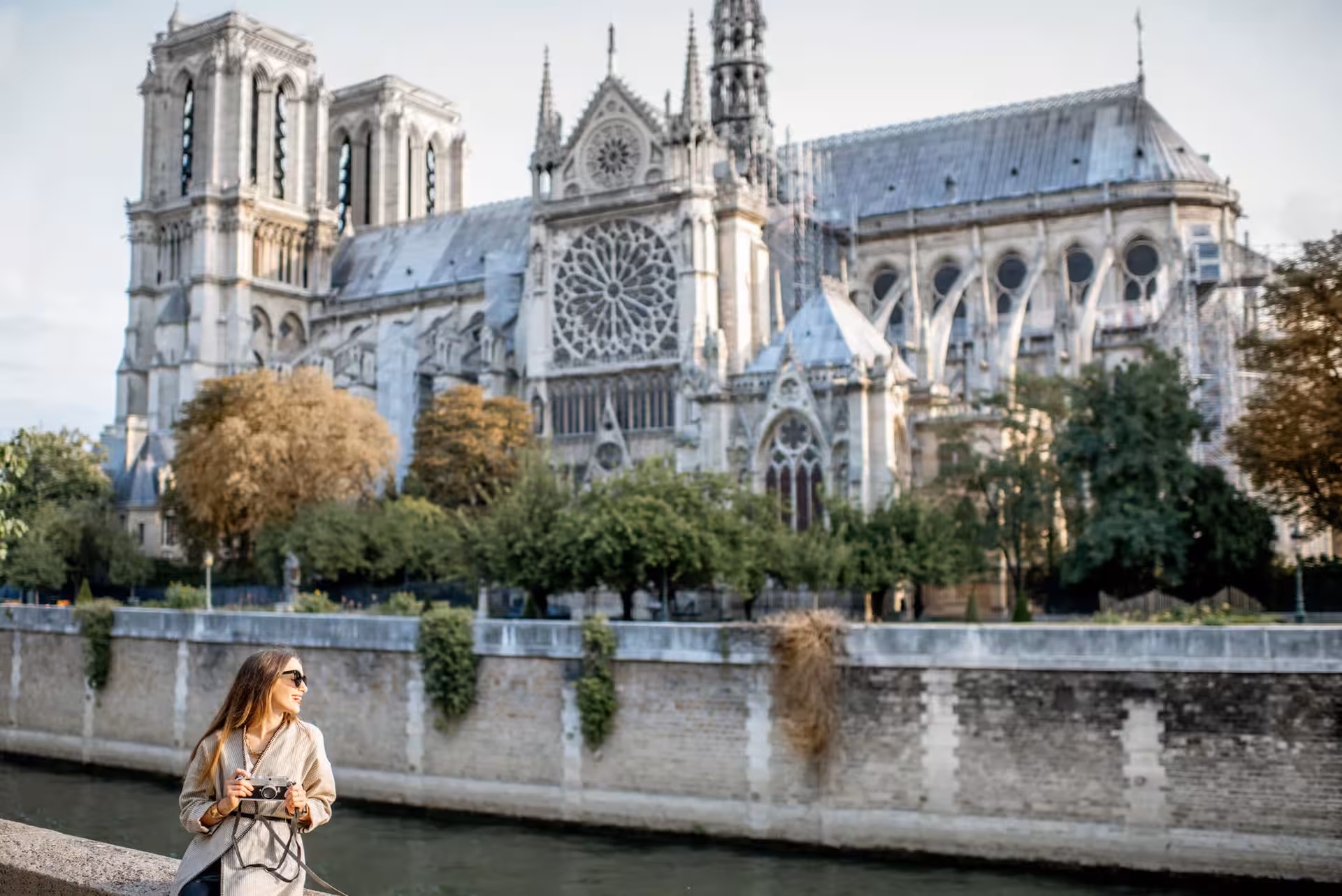 Female tourist with camera posing by the Seine River with Notre-Dame Cathedral in Paris background