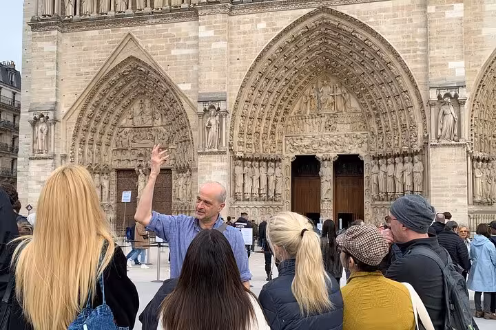 Tour guide gesturing to group of tourists in front of Notre-Dame Cathedral ornate Gothic facade, Paris