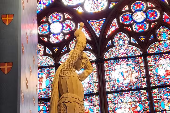 Stone statue by colorful rose stained glass on a small-group Notre Dame interior guided tour in Paris