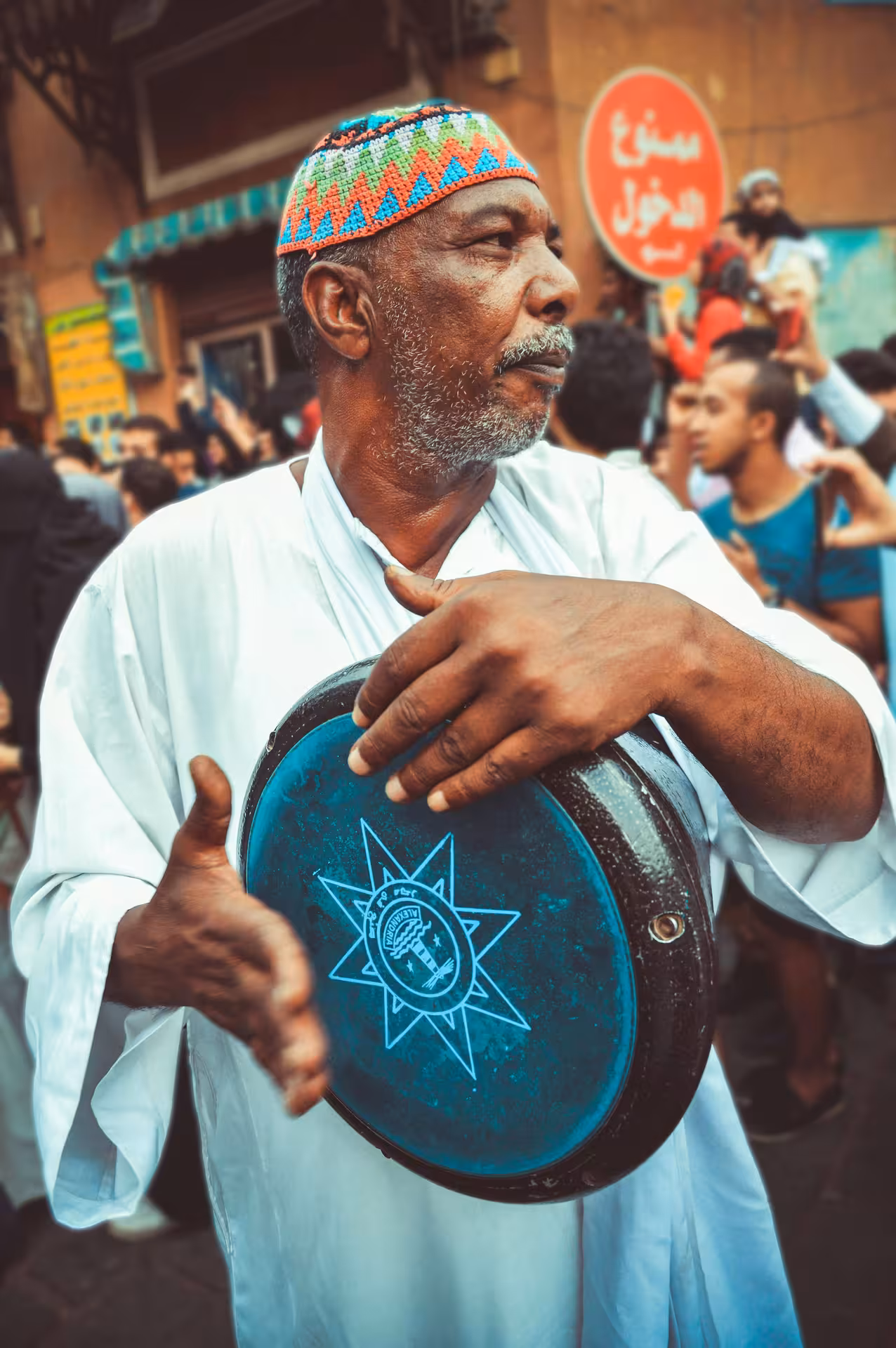 Nubian man in white thobe and colorful cap playing traditional drum at Aswan street festival