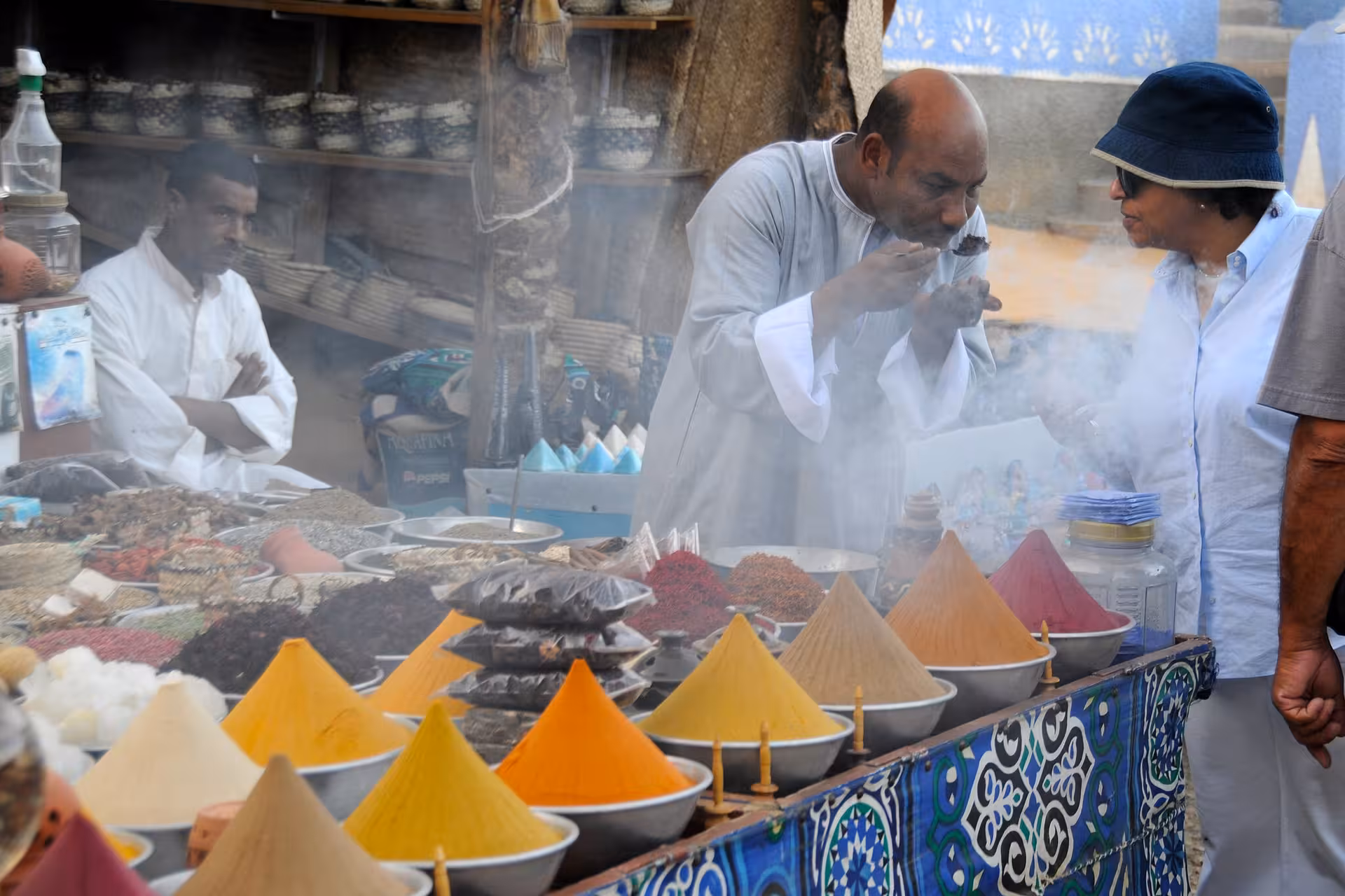 Vendor demonstrating colorful spices at a Nubian market stall in Aswan with smoke rising