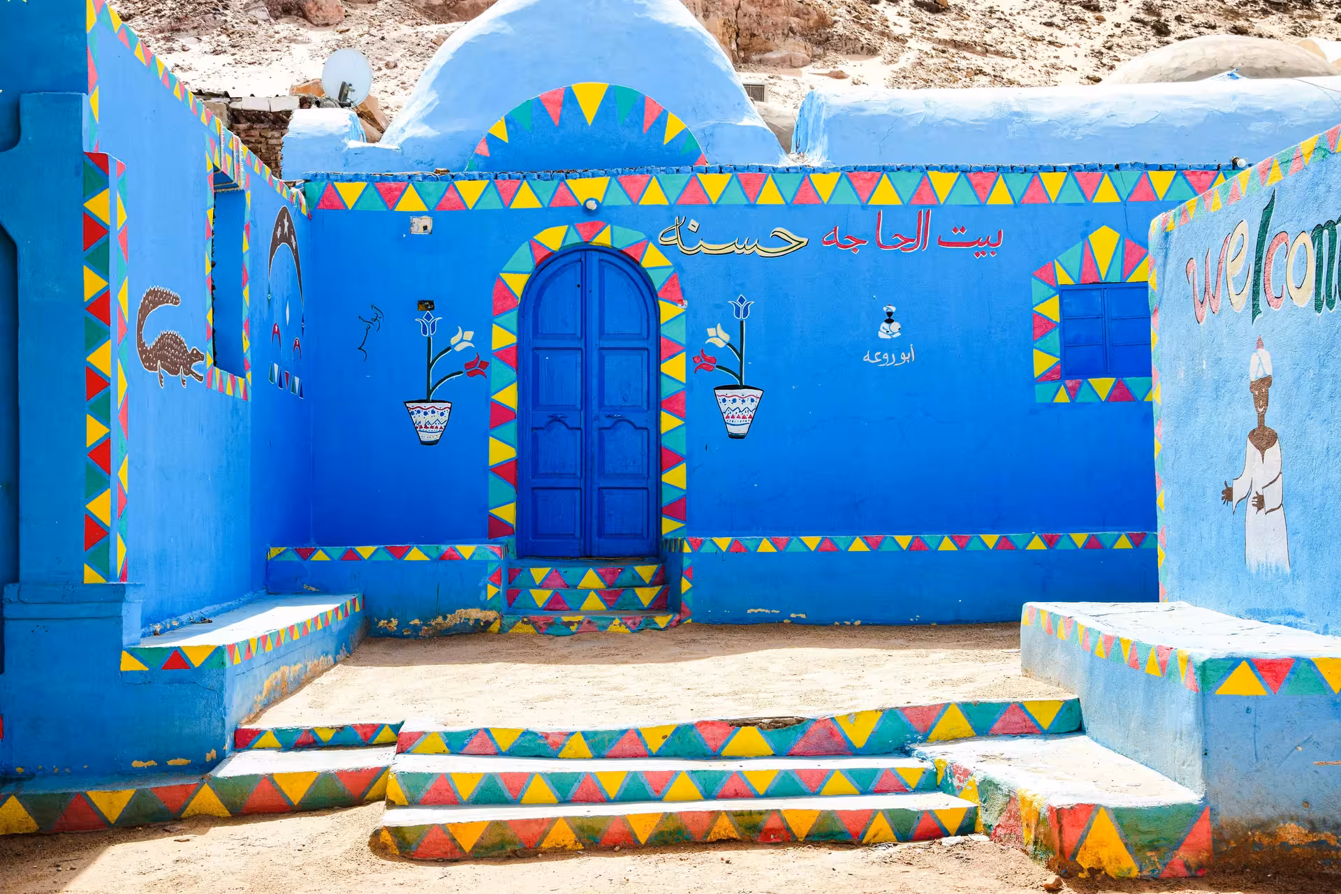 Colorful blue Nubian house with Arabic script and geometric murals in Aswan village