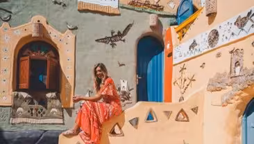 Woman in red dress sitting on colorful Nubian village steps with traditional painted walls in Aswan