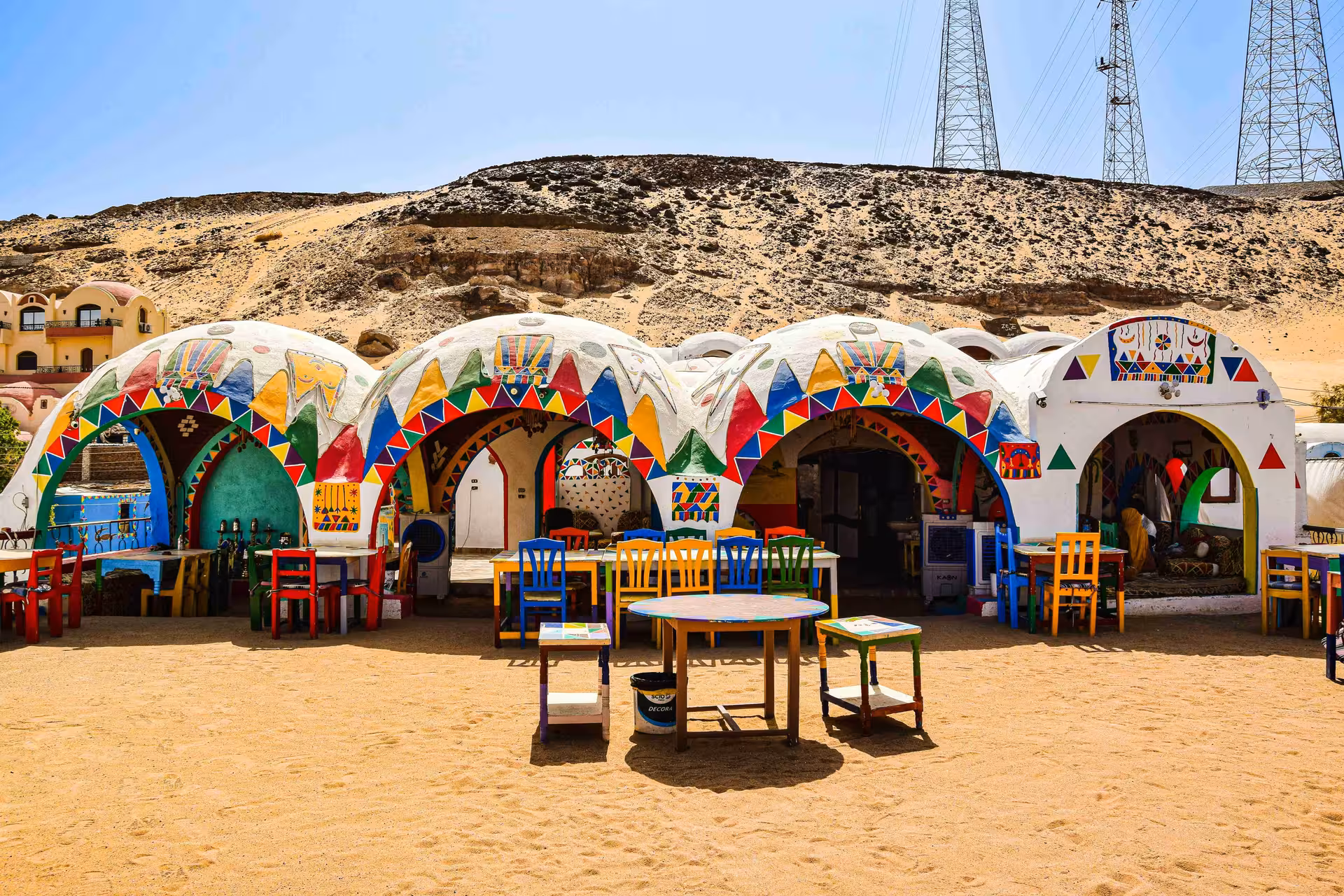 Colorful dome-shaped Nubian village buildings with vibrant geometric murals and painted chairs in Aswan desert