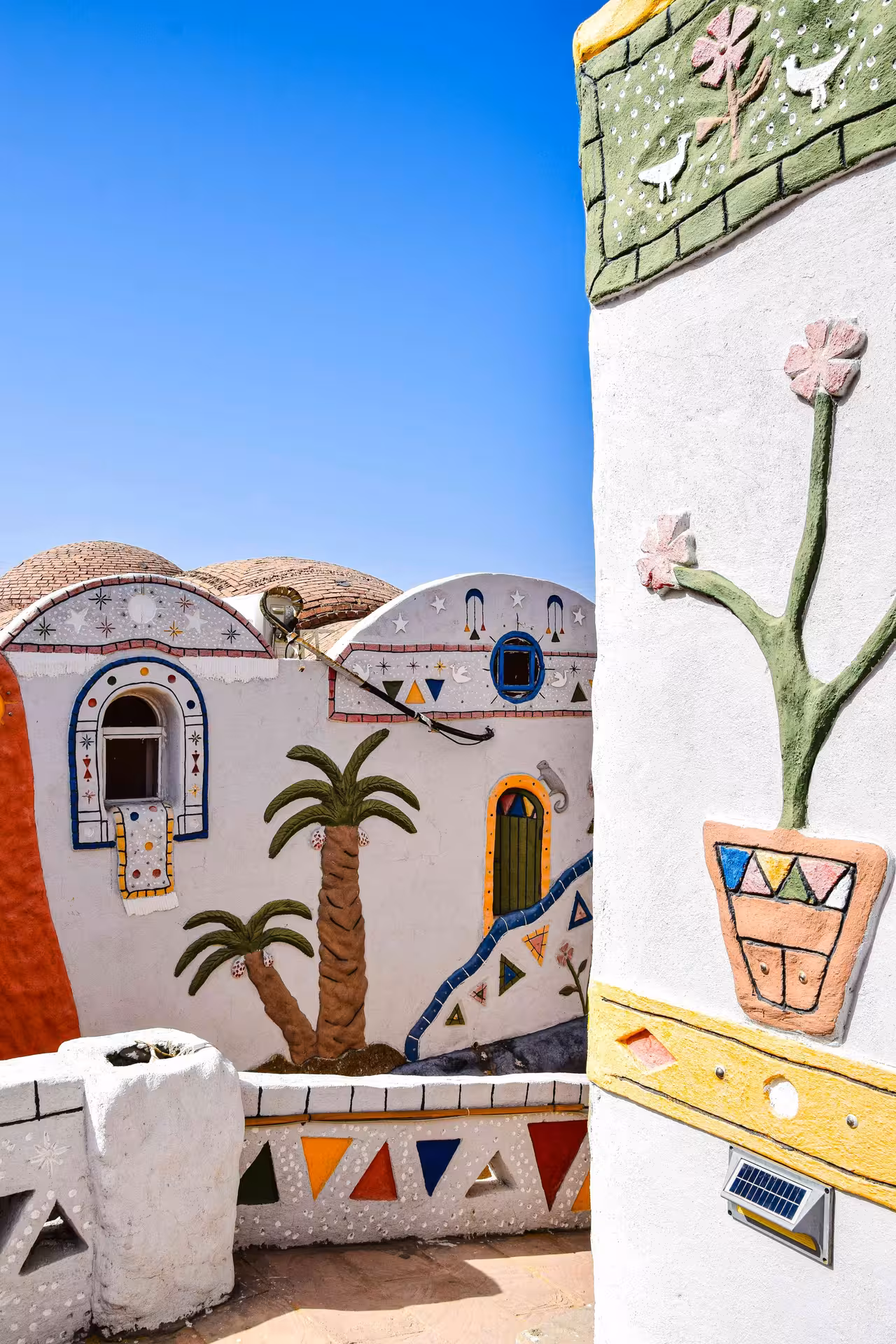 Colorful Nubian village buildings with traditional painted murals, palm trees, and domed rooftops in Aswan, Egypt