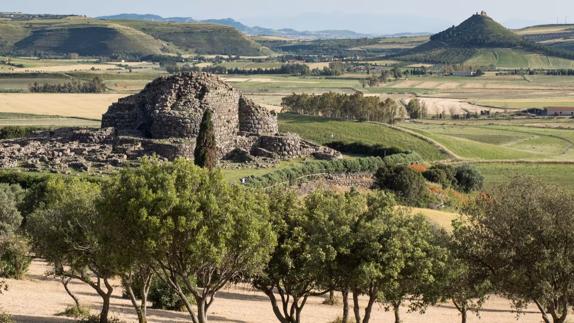 The ancient Nuraghe Su Nuraxi at Barumini, a UNESCO site, stands amidst Sardinia's lush, rolling landscape.