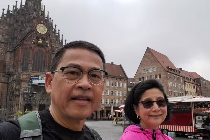 Couple posing for selfie in Nuremberg's main market square with Church of Our Lady clock tower behind