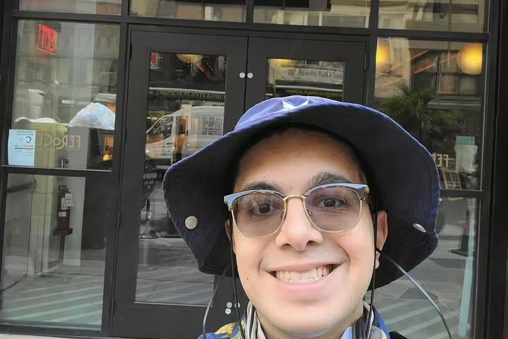 Smiling man wearing blue bucket hat and glasses on NYC street during self-guided outdoor tour