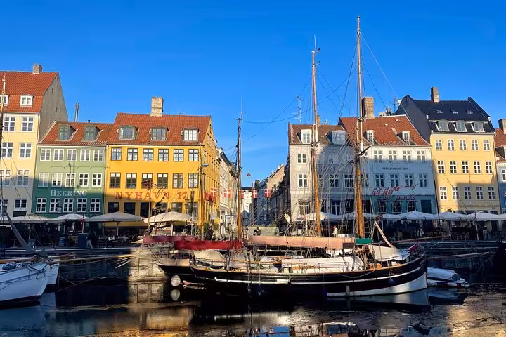 Colorful historic buildings and boats at Nyhavn canal in Copenhagen under a clear blue sky.