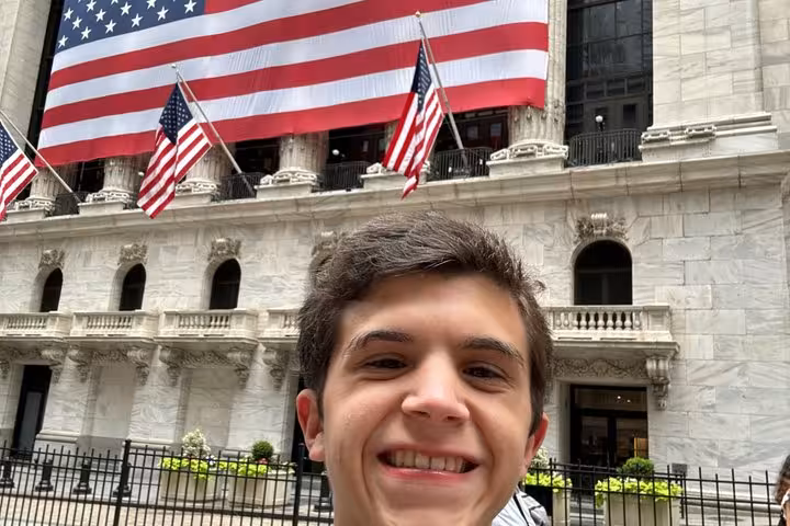 Young man smiling in selfie in front of New York Stock Exchange with American flags, Lower Manhattan NYC