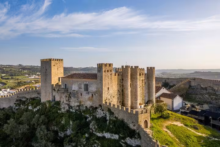 Aerial view of the medieval Óbidos Castle surrounded by picturesque landscape and blue sky.