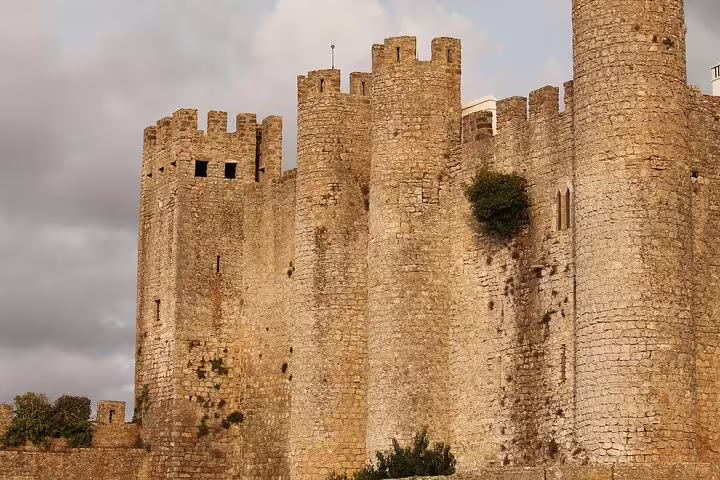 Majestic view of Óbidos Castle under cloudy skies, highlighting the historic architecture on the Fátima and Óbidos Day Tour.