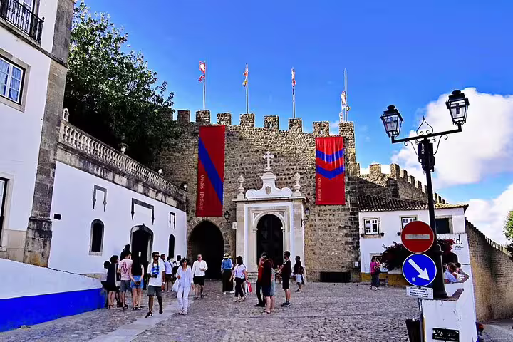 Tourists explore the historic entrance of Óbidos Castle, a key stop on the Porto to Lisbon tour route.