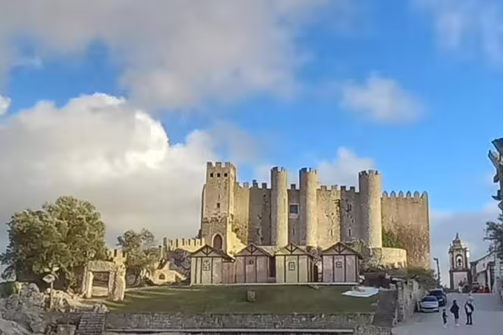 Majestic Obidos Castle in Portugal under a bright blue sky, surrounded by medieval architecture and lush greenery.