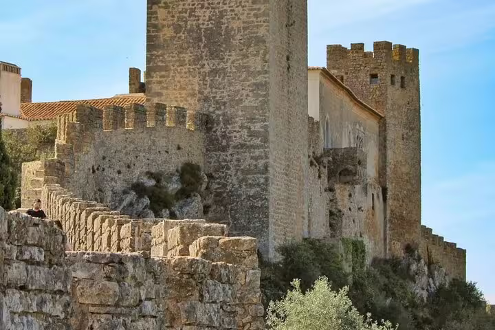 Ancient stone walls and towers of Óbidos Castle under a clear blue sky, featured in the Fátima, Nazaré, and Óbidos full-day tour.