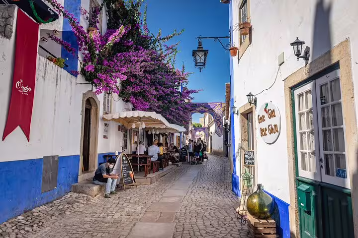 Cobbled street in Óbidos with bougainvillea and cafés, stop on Lisbon to Fátima Nazaré tour