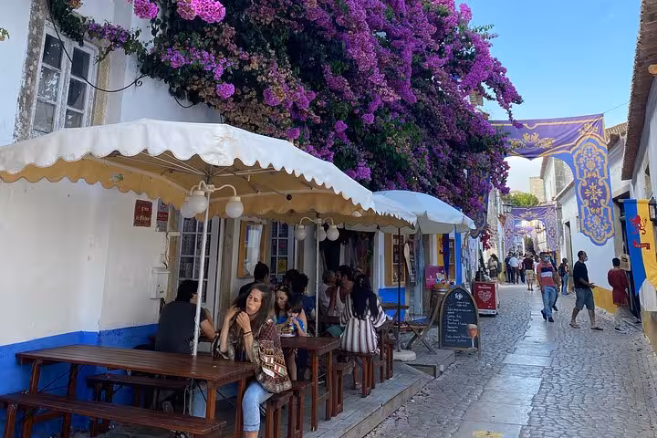 Charming cobblestone street in Obidos lined with vibrant bougainvillea and outdoor cafes bustling with visitors.