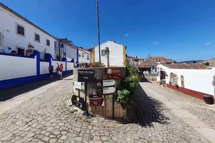 Charming cobblestone street in Óbidos with colorful buildings and signposts, featured on the Fátima, Batalha, Nazaré & Óbidos Private Tour.
